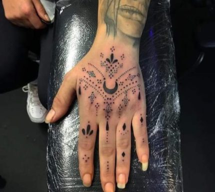 A hand adorned with intricate black tattoos featuring floral and geometric designs.