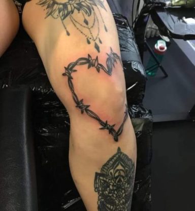 Tattoo on a leg showing a heart shape surrounded by barbed wire and decorative elements.