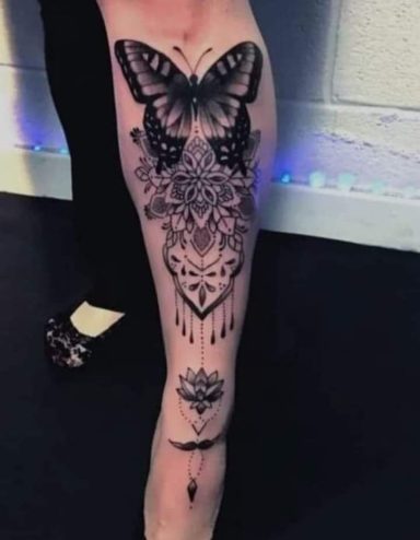 Black and grey tattoo of a butterfly with intricate patterns on a leg.