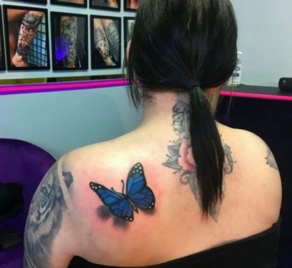 Blue butterfly tattoo on the upper back, surrounded by floral designs.