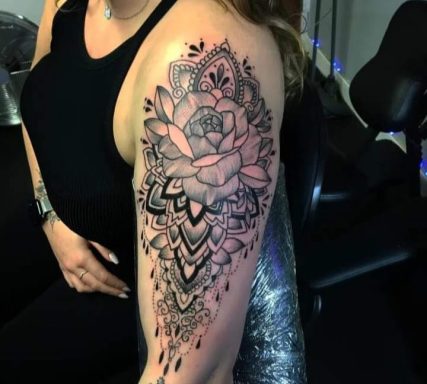 Black and grey floral tattoo covering the upper arm, featuring intricate designs.