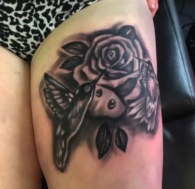 Black and grey tattoo of a rose and hummingbirds on a thigh.