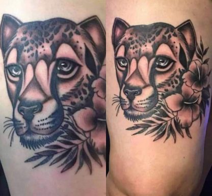 Tattoo of a leopard's head surrounded by flowers and foliage.