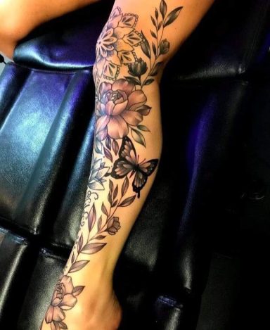 A detailed black and grey tattoo featuring flowers and a butterfly on a leg.