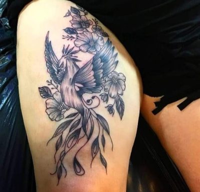 A detailed tattoo of a phoenix among flowers on a thigh.