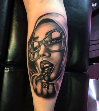 Black and grey tattoo of a woman wearing glasses, holding a cigarette in her fist.