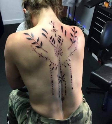 Decorative black tattoo design featuring intricate patterns and leaf motifs on a person's back.