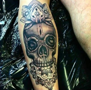Tattoo of a skull adorned with floral designs on the forearm.