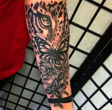 A detailed tattoo featuring a leopard's eye, a butterfly, and floral designs.