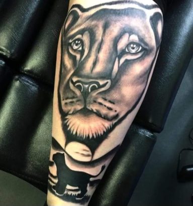 Black and grey tattoo of a lioness and a silhouette of a smaller dog.