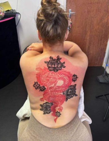 A detailed tattoo of a red dragon surrounded by black floral designs on a person's back.