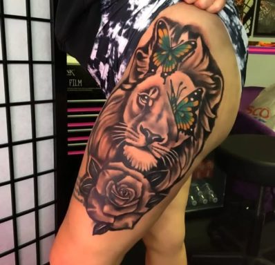 A detailed lion tattoo with butterflies and a rose on the thigh.
