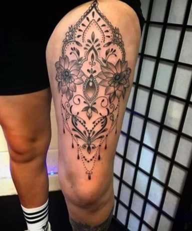 Black intricate floral tattoo design on a thigh, featuring symmetrical patterns and details.