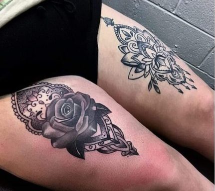 Black and grey floral tattoos featuring a rose and intricate mandala designs on thighs.