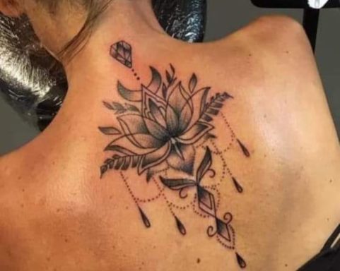 Black and grey lotus flower tattoo with decorative elements on a person's back.