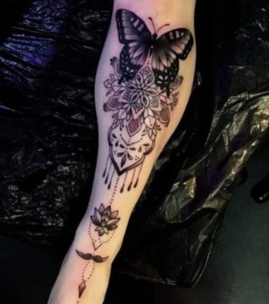 Black and grey tattoo of a butterfly, flowers, and geometric patterns on a forearm.