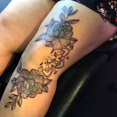 Tattoo of large flowers and intricate patterns on a thigh.