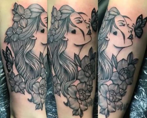 A woman with flowing hair, surrounded by flowers and a butterfly, depicted in a tattoo.